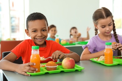 Photo of Children sitting at table and eating healthy food during break at school