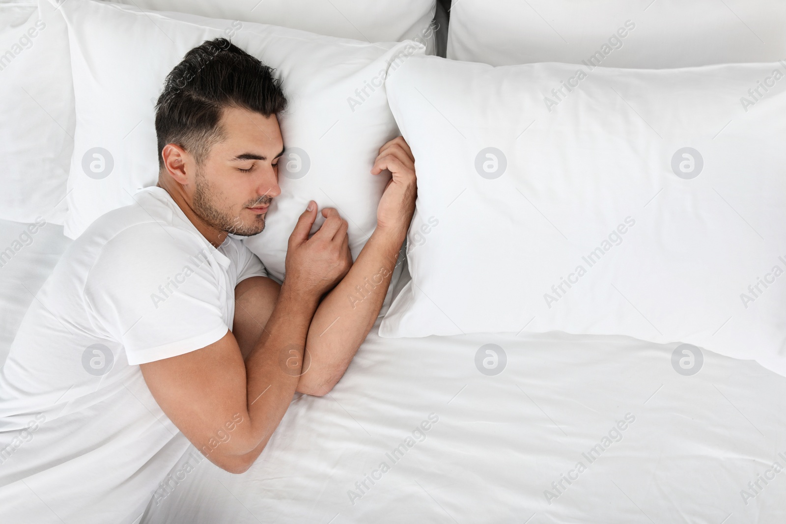 Photo of Young man sleeping on bed with soft pillows at home, top view