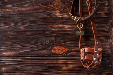Photo of Brown leather dog muzzle and collar on wooden table, top view. Space for text