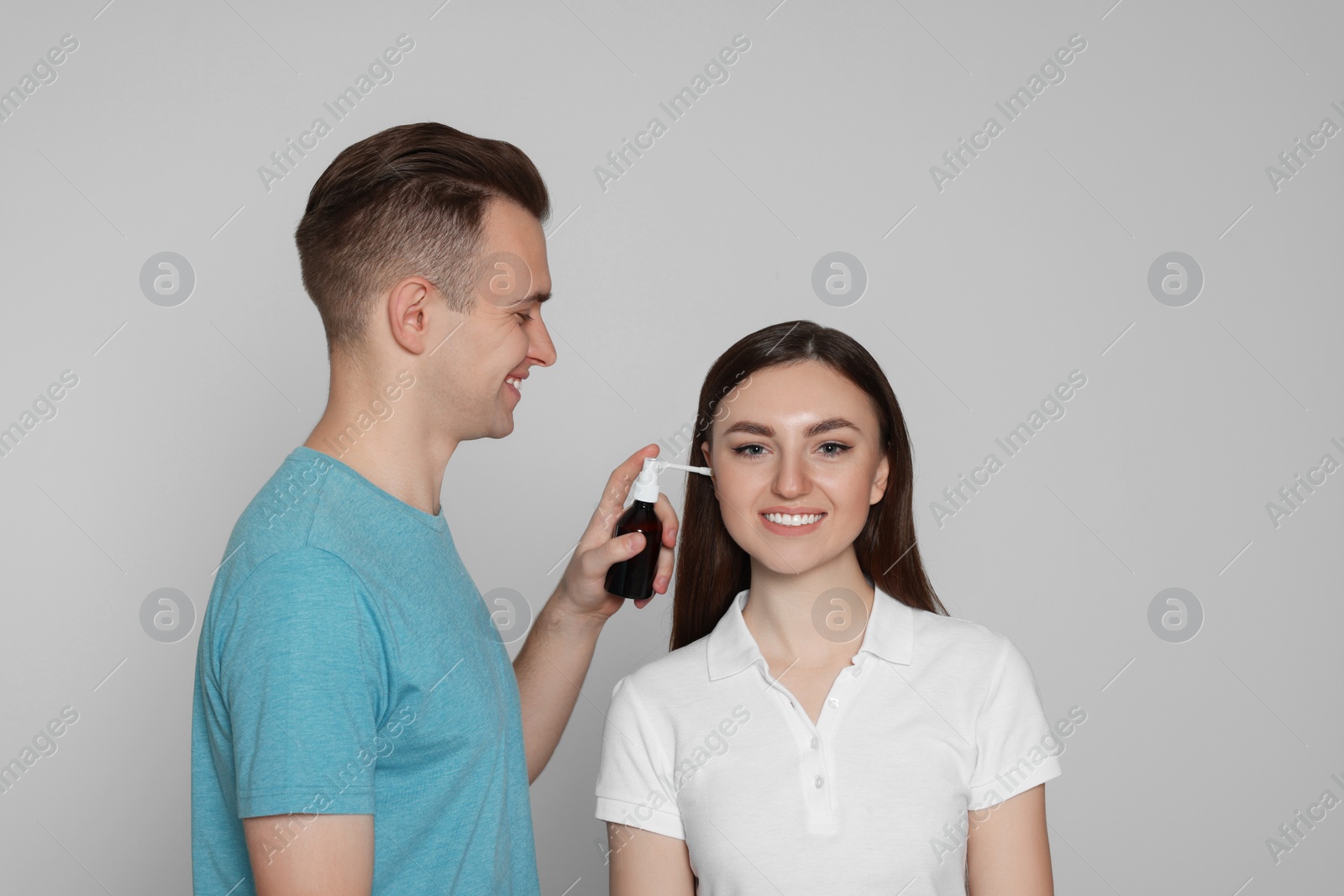 Photo of Man spraying medication into woman`s ear on light grey background