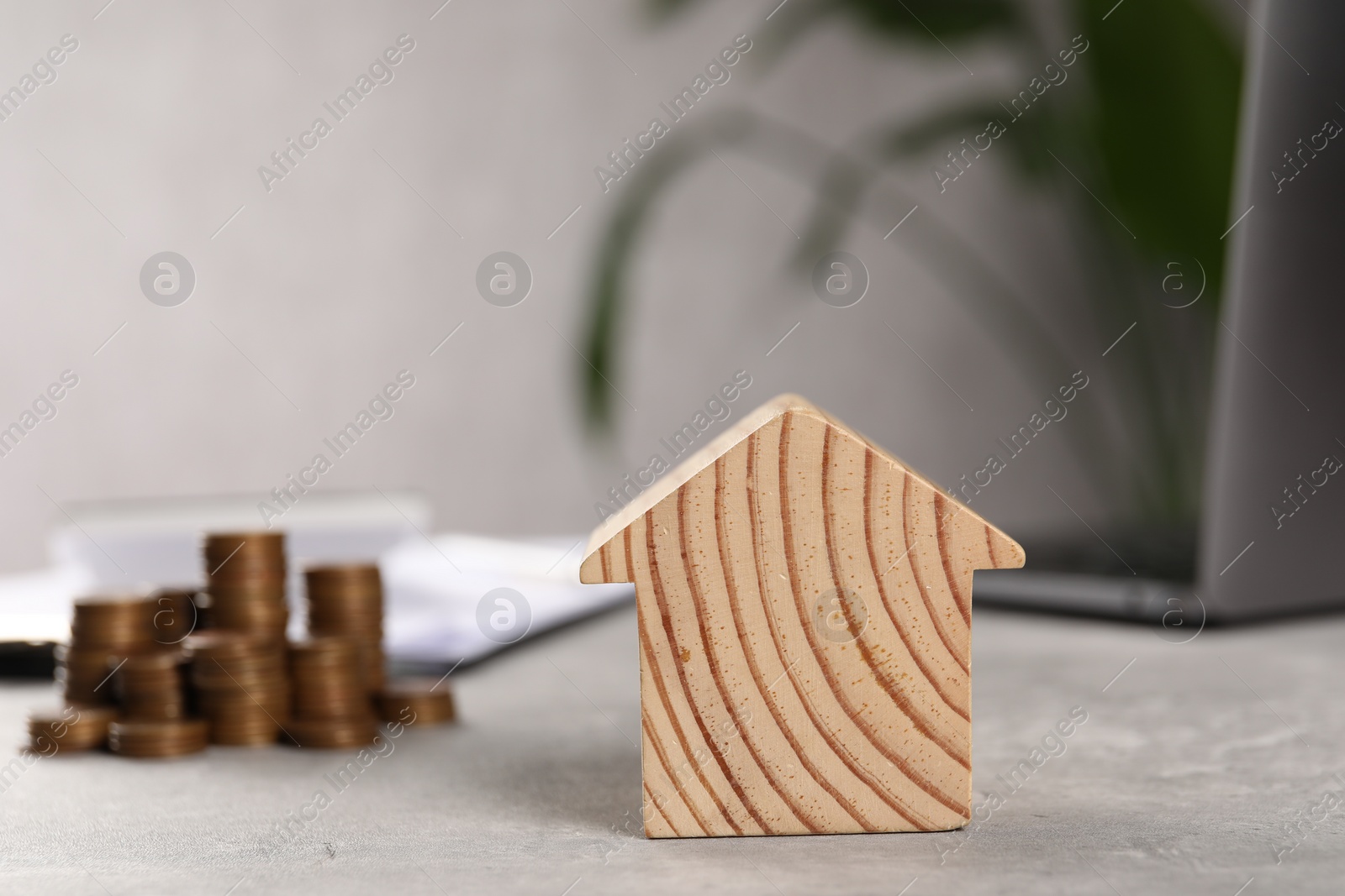 Photo of House model, stacked coins, laptop and clipboard on grey table, selective focus