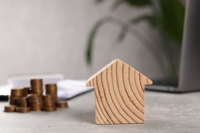 Photo of House model, stacked coins, laptop and clipboard on grey table, selective focus