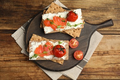 Photo of Fresh rye crispbreads with salmon, cream cheese and tomatoes on wooden table, top view