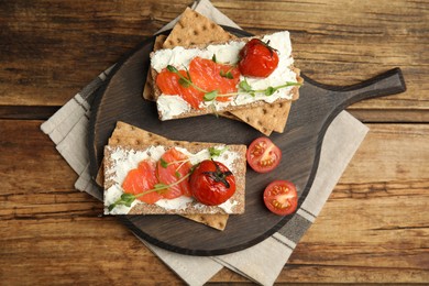 Fresh rye crispbreads with salmon, cream cheese and tomatoes on wooden table, top view