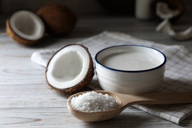 Photo of Bowl of delicious coconut milk, spoon with flakes and nuts on white wooden table, closeup