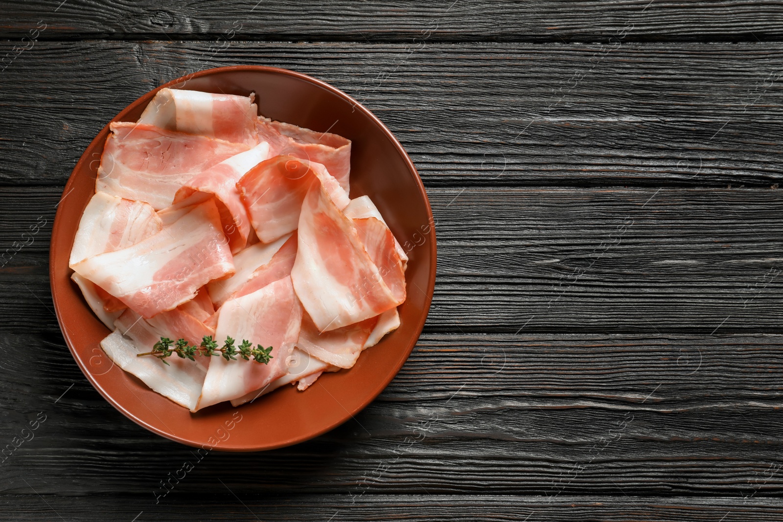 Photo of Plate with raw bacon rashers on wooden background