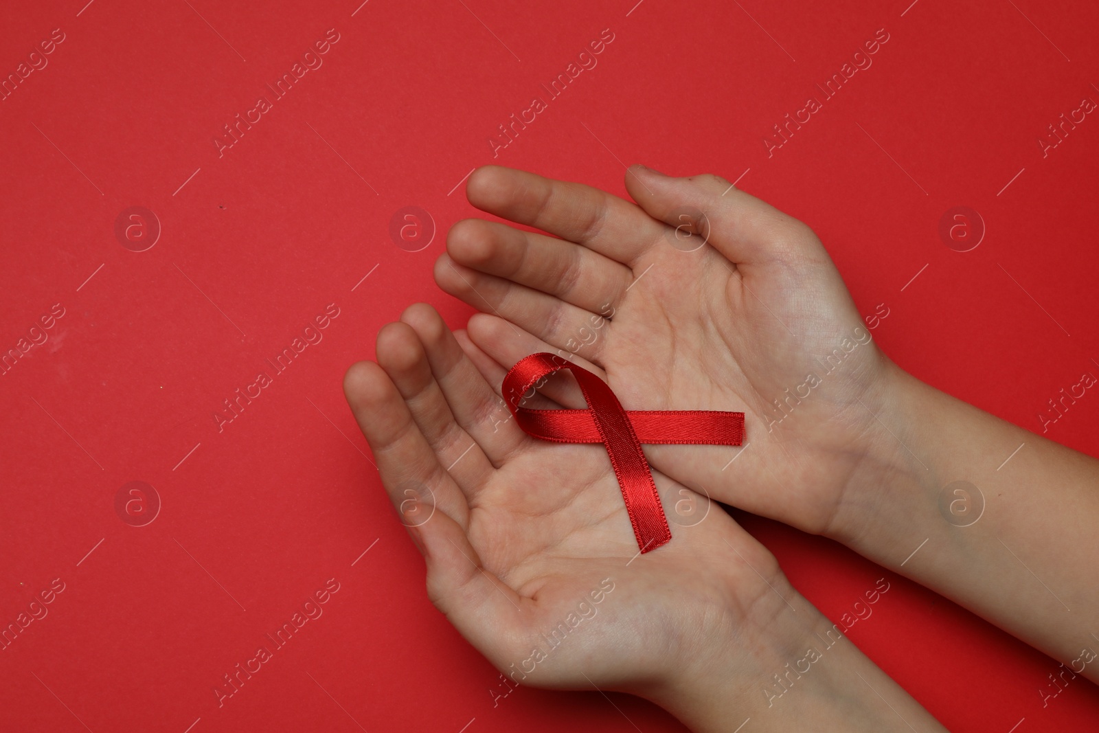 Photo of Little girl holding red ribbon on bright background, top view. AIDS disease awareness