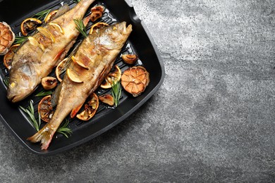Photo of Tasty homemade roasted perches in grill pan on grey table, top view and space for text. River fish