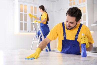 Photo of Professional young janitor cleaning table in kitchen