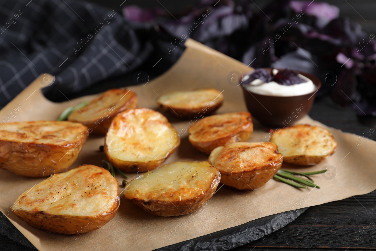 Photo of Delicious potato wedges with sour cream on black wooden table, closeup