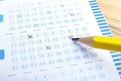 Filling out lottery ticket with pencil on wooden table, closeup. Space for text