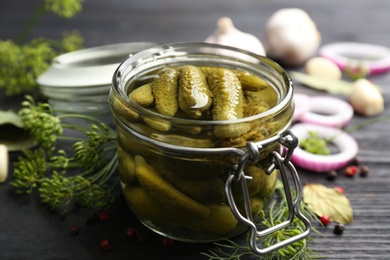 Glass jar of pickled cucumbers and ingredients on black wooden table, closeup