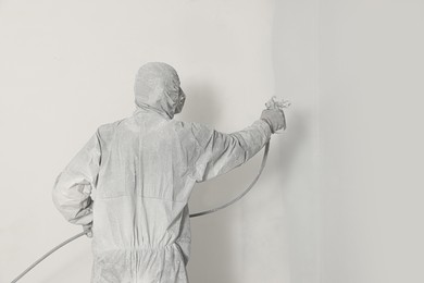Decorator in uniform painting wall with sprayer indoors, back view