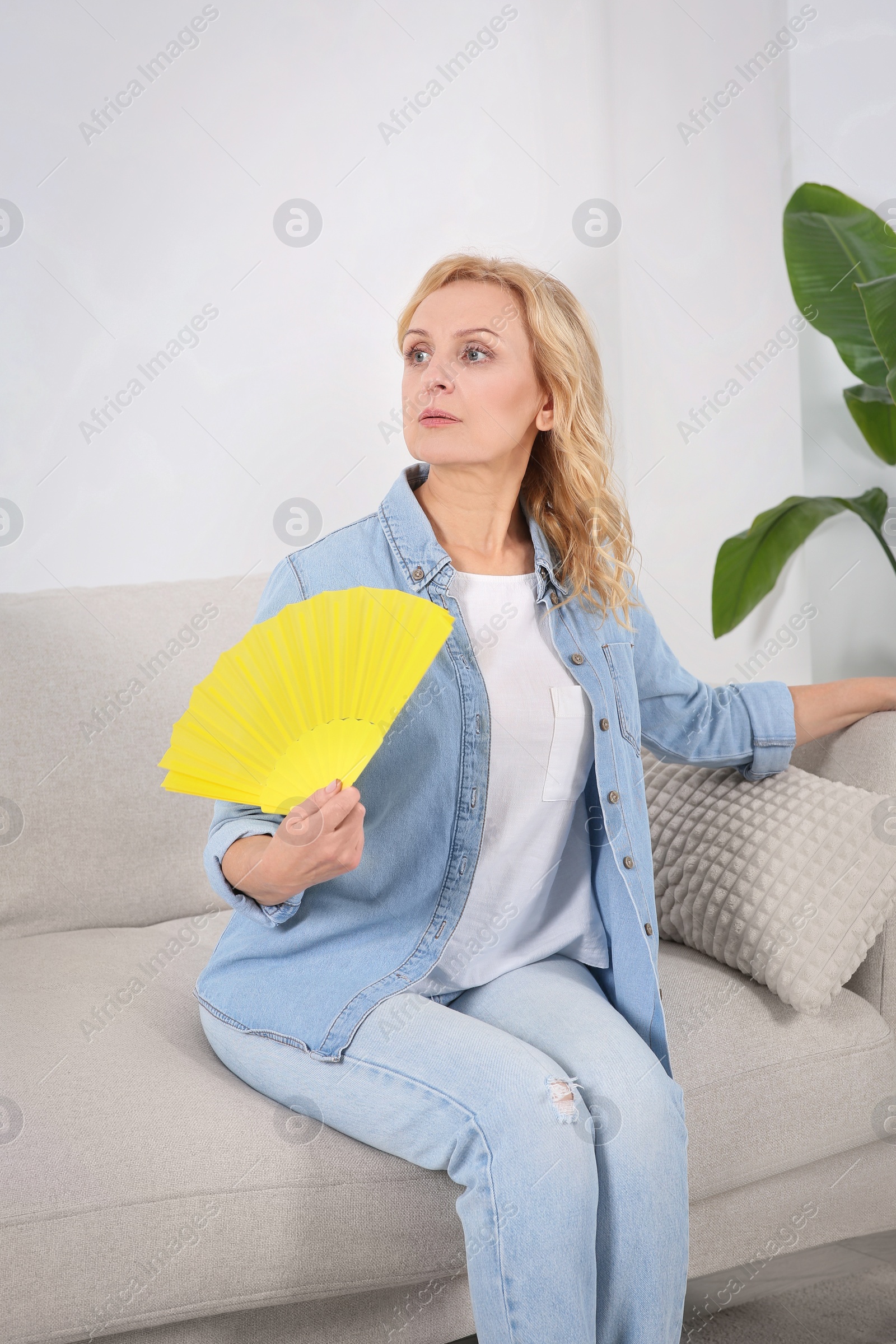 Photo of Woman waving hand fan to cool herself at home. Hormonal disorders