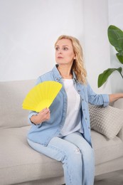 Woman waving hand fan to cool herself at home. Hormonal disorders