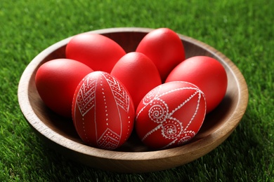 Photo of Wooden bowl with red painted Easter eggs on green grass