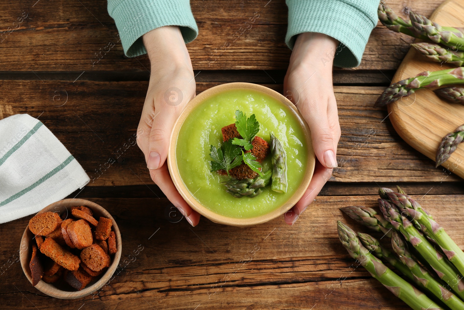 Photo of Woman with bowl of asparagus soup at wooden table, top view