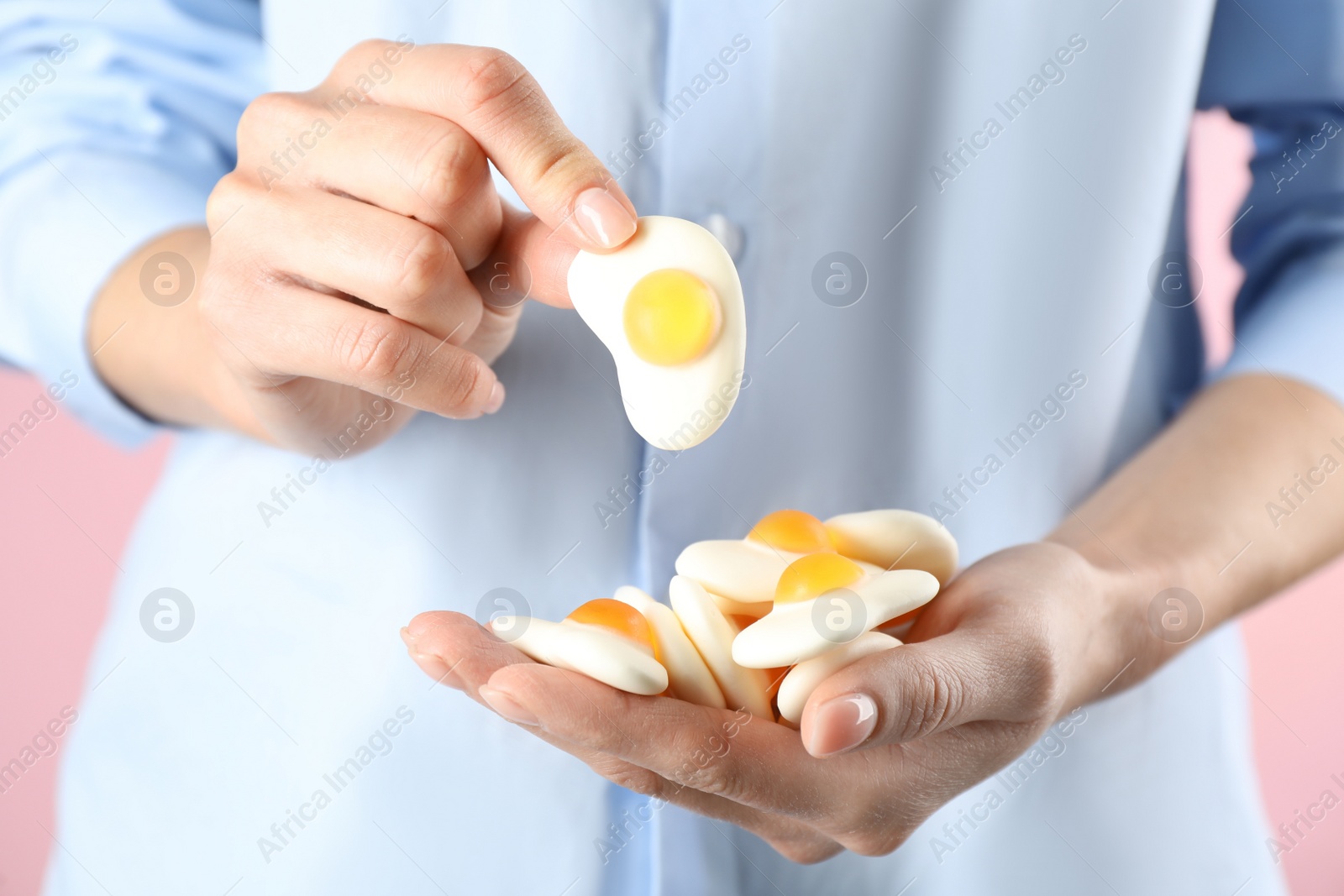 Photo of Woman holding handful of delicious gummy fried eggs shaped candies on pink background, closeup