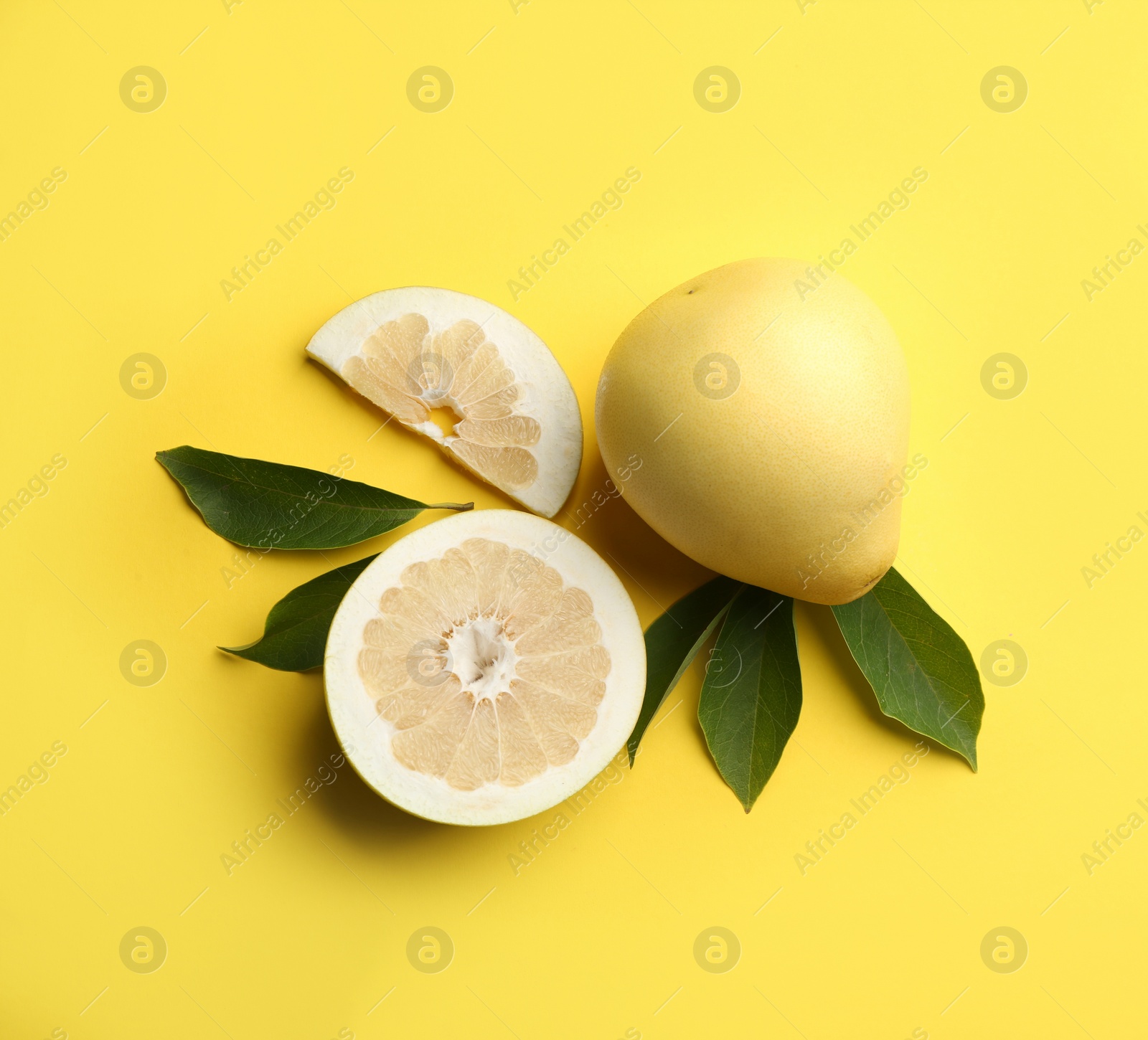 Photo of Fresh cut and whole pomelo fruits with leaves on yellow background, flat lay