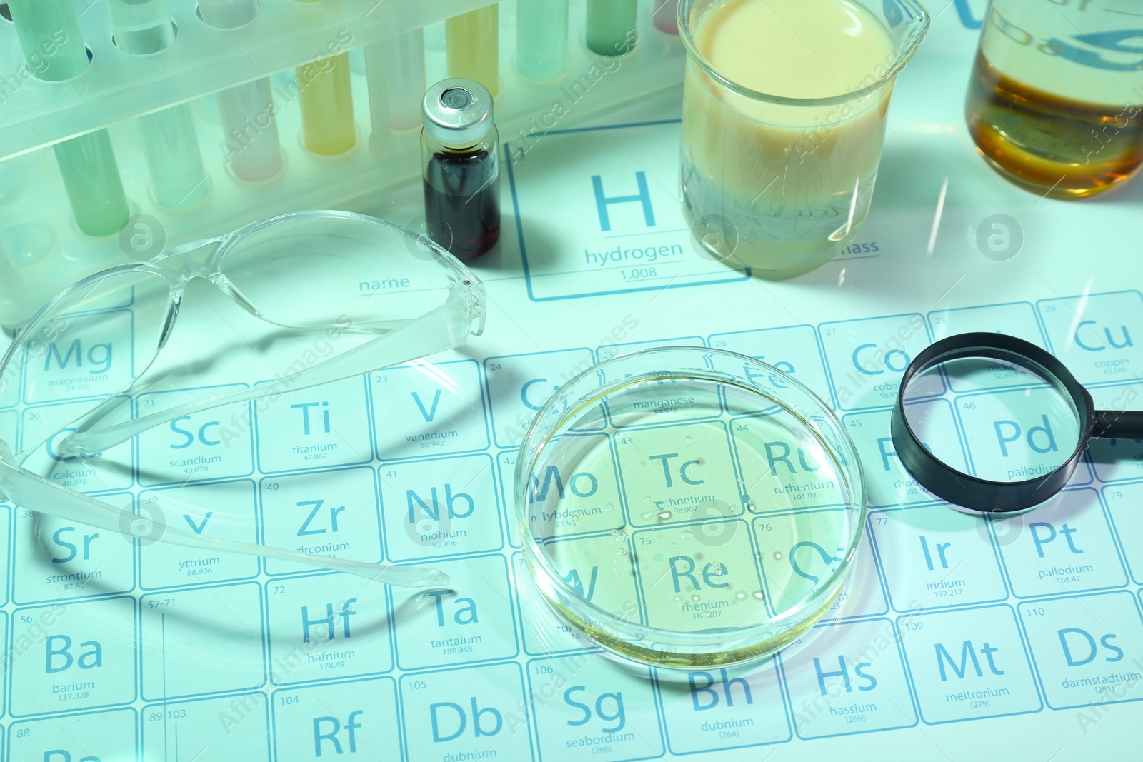 Photo of Different laboratory equipment with liquids and safety glasses on periodic table of chemical elements. Light green tone effect