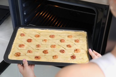 Photo of Woman putting baking pan with baklava into oven, closeup
