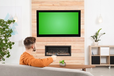 Photo of Man watching TV on sofa in living room with decorative fireplace