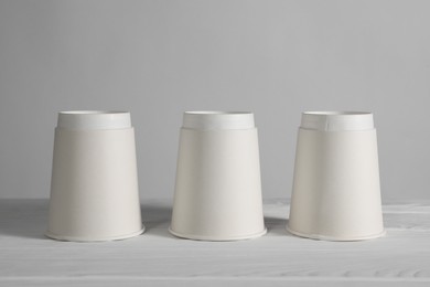 Photo of Shell game. Three paper cups on white wooden table