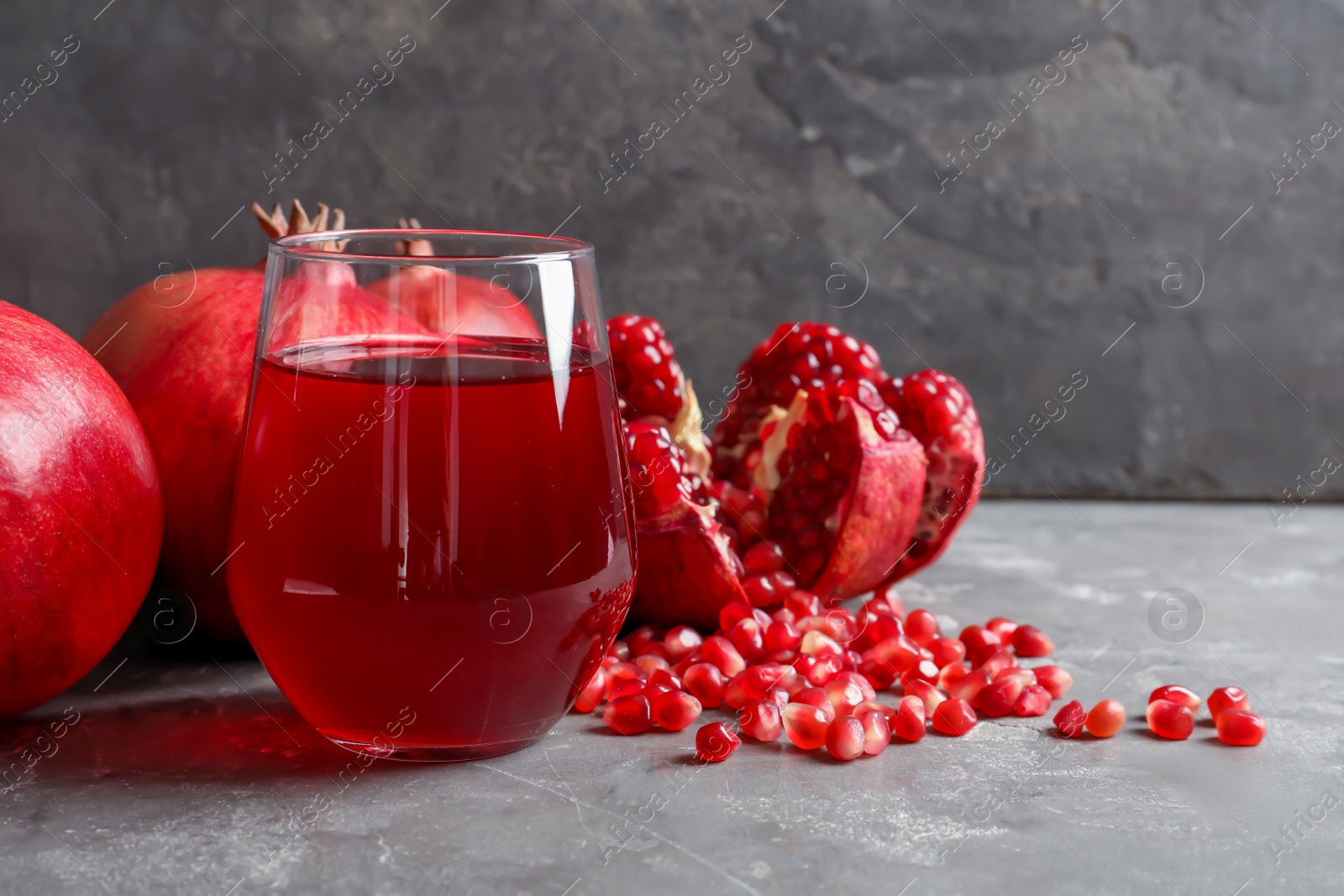 Photo of Glass of pomegranate juice and fresh fruits on table against grey background