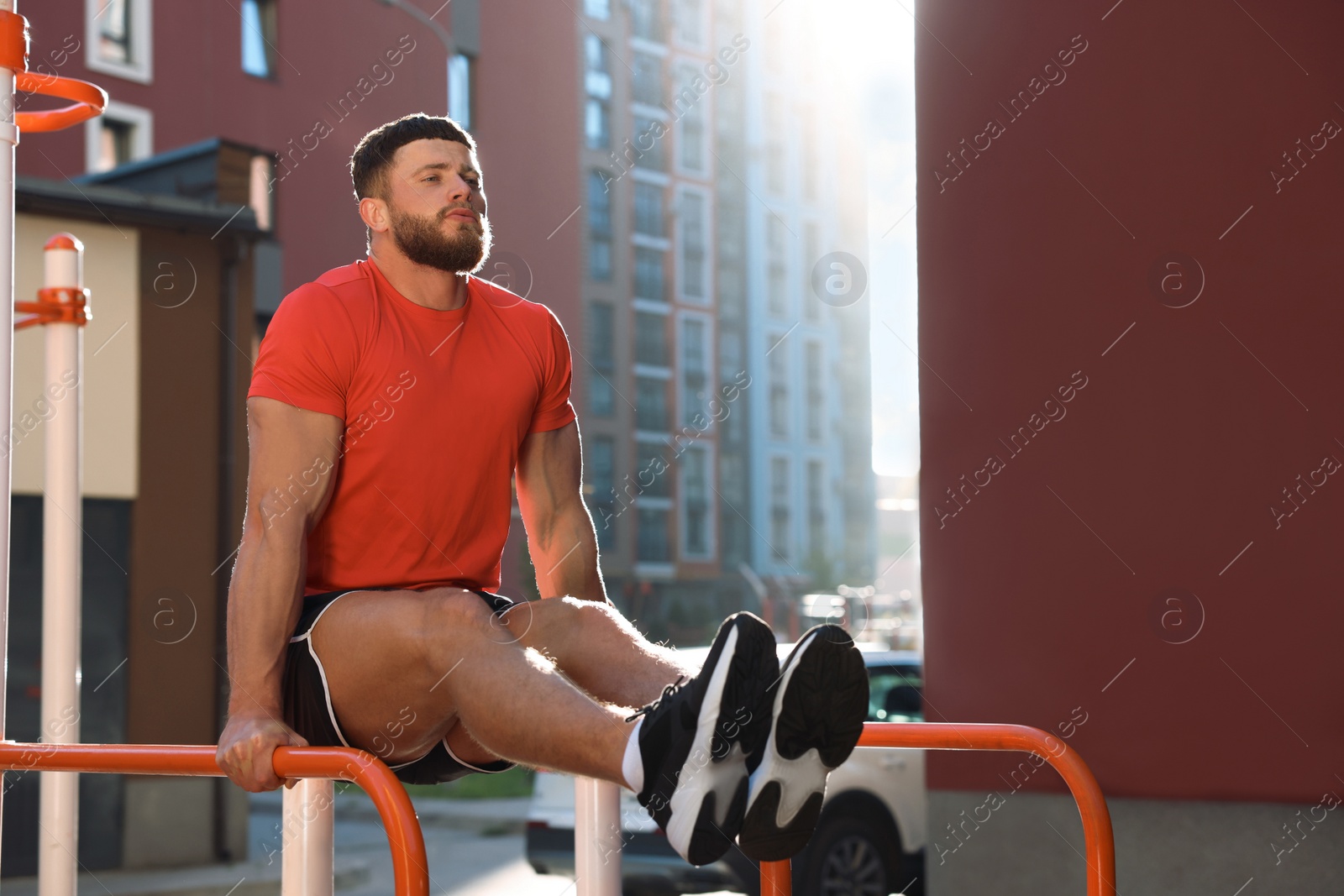 Photo of Man training on parallel bars at outdoor gym on sunny day