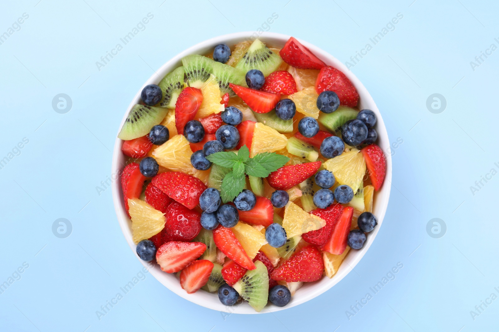 Photo of Yummy fruit salad in bowl on light blue background, top view