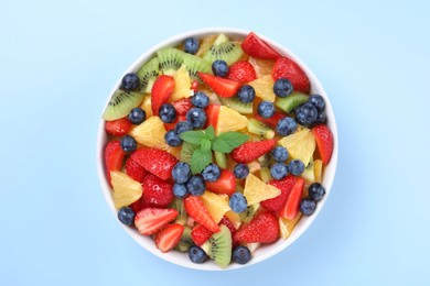 Yummy fruit salad in bowl on light blue background, top view