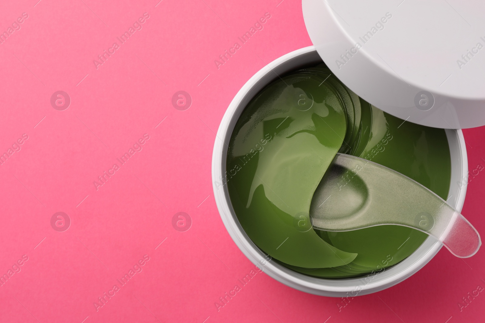 Photo of Jar of under eye patches and spoon on pink background, top view with space for text. Cosmetic product