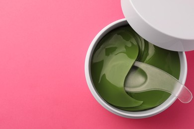 Photo of Jar of under eye patches and spoon on pink background, top view with space for text. Cosmetic product