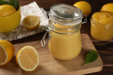 Photo of Delicious lemon curd in glass jars, fresh citrus fruits and green leaf on wooden table
