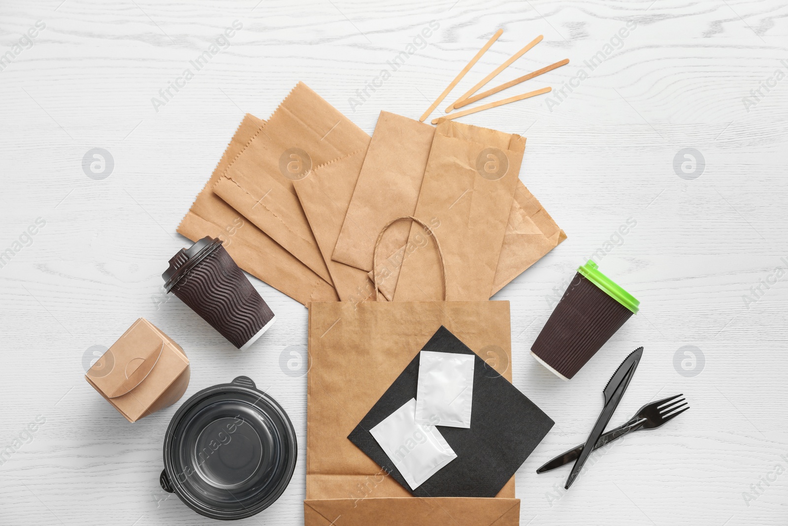 Photo of Flat lay composition with paper bags and different takeaway items on wooden background. Space for design