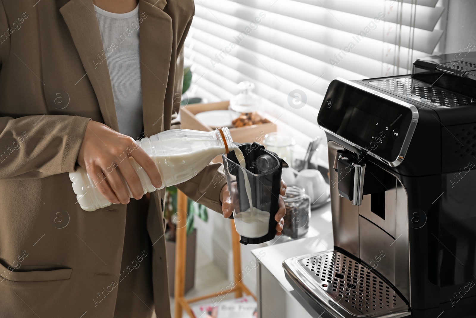 Photo of Young woman pouring milk into container near modern coffee machine in office, closeup