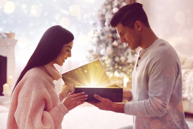 Image of Couple opening Christmas gift with magic light at home. Bokeh effect