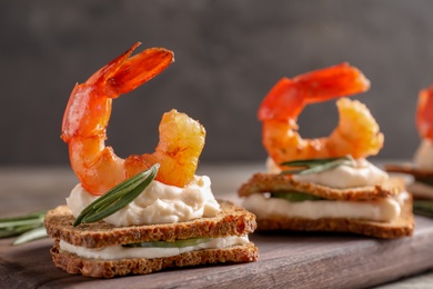 Photo of Delicious small sandwiches with shrimps on wooden board