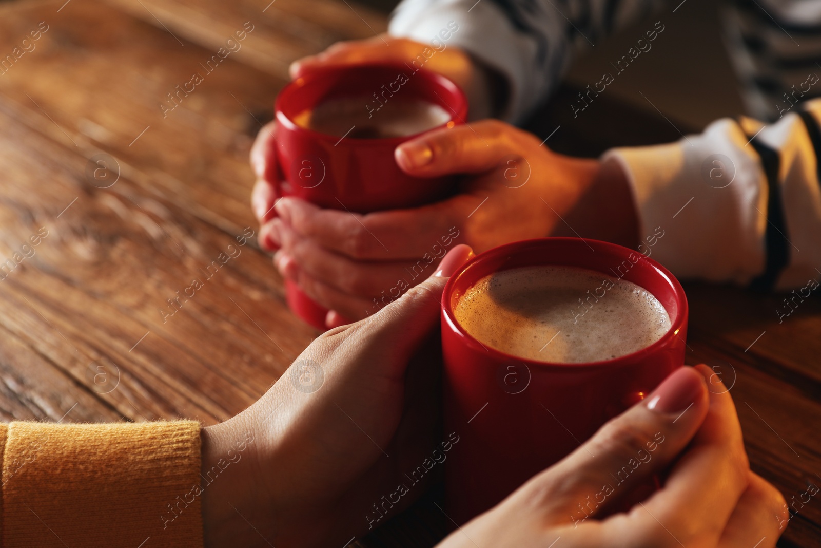 Photo of Women with mugs of hot coffee at wooden table, closeup