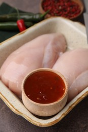 Photo of Marinade and raw chicken fillets on brown table, closeup