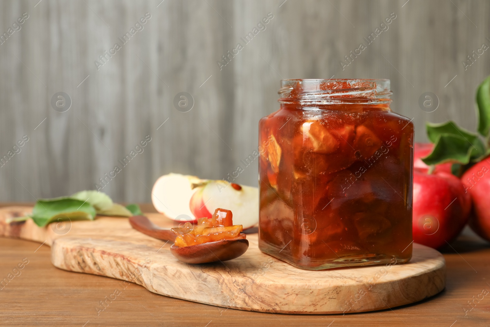 Photo of Tasty apple jam in glass jar and fresh fruits on wooden table, space for text