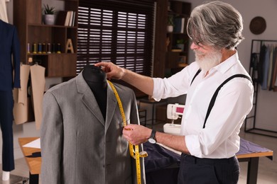 Photo of Professional tailor with measuring tape working in atelier