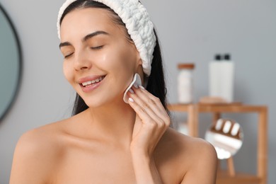 Photo of Young woman using cotton pad with micellar water indoors