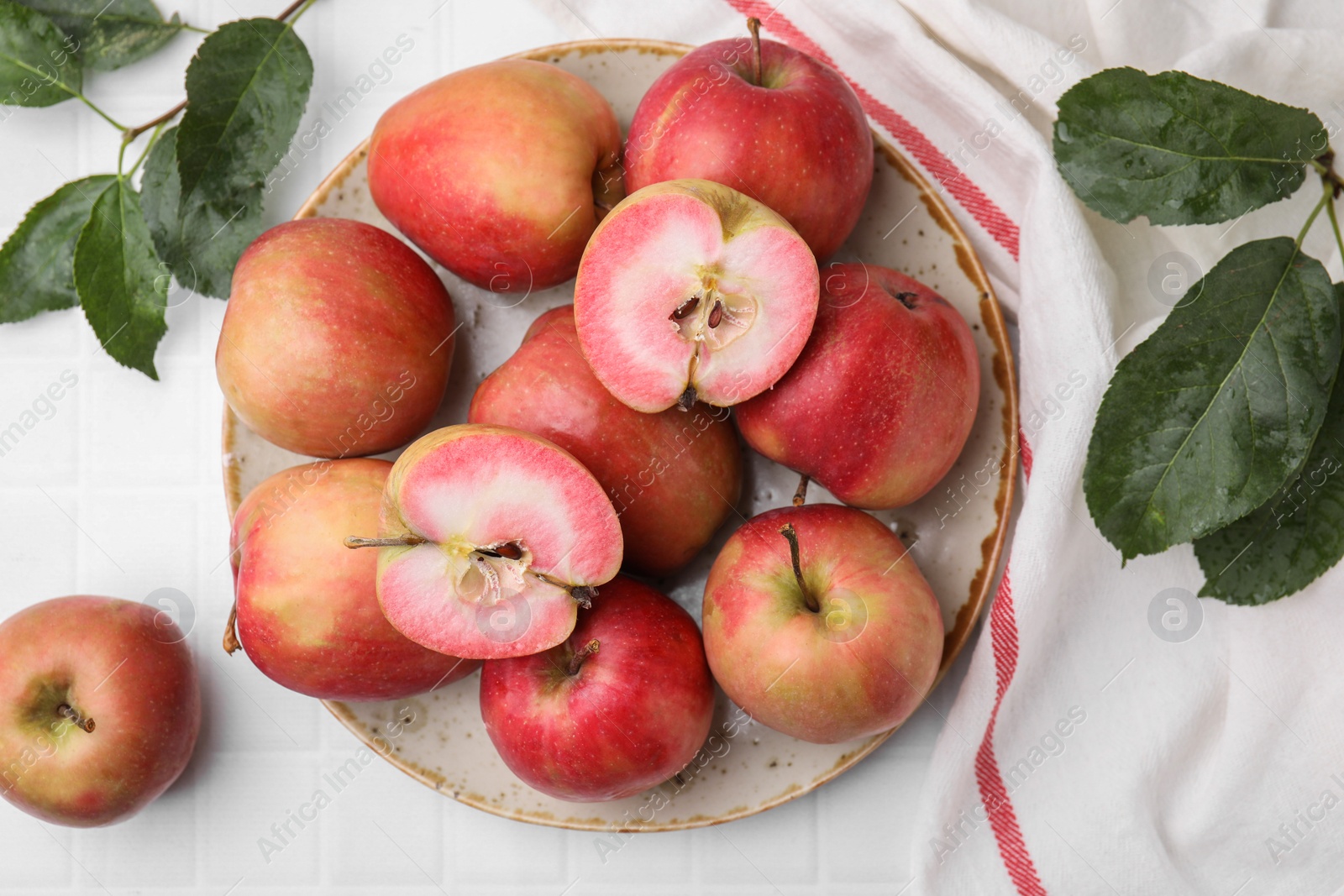 Photo of Tasty apples with red pulp and leaves on white tiled table, flat lay