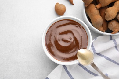 Photo of Bowl of tamarind sauce, spoon and fresh pods on light table, flat lay. Space for text