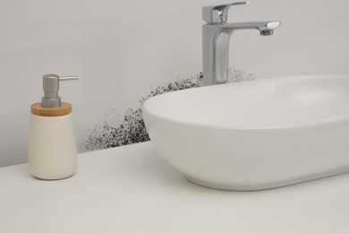 Image of White wall affected with mold. White washbasin and soap dispenser in bathroom