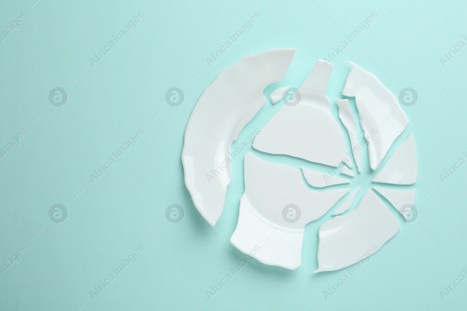 Photo of Pieces of broken ceramic plate on light blue background, flat lay. Space for text