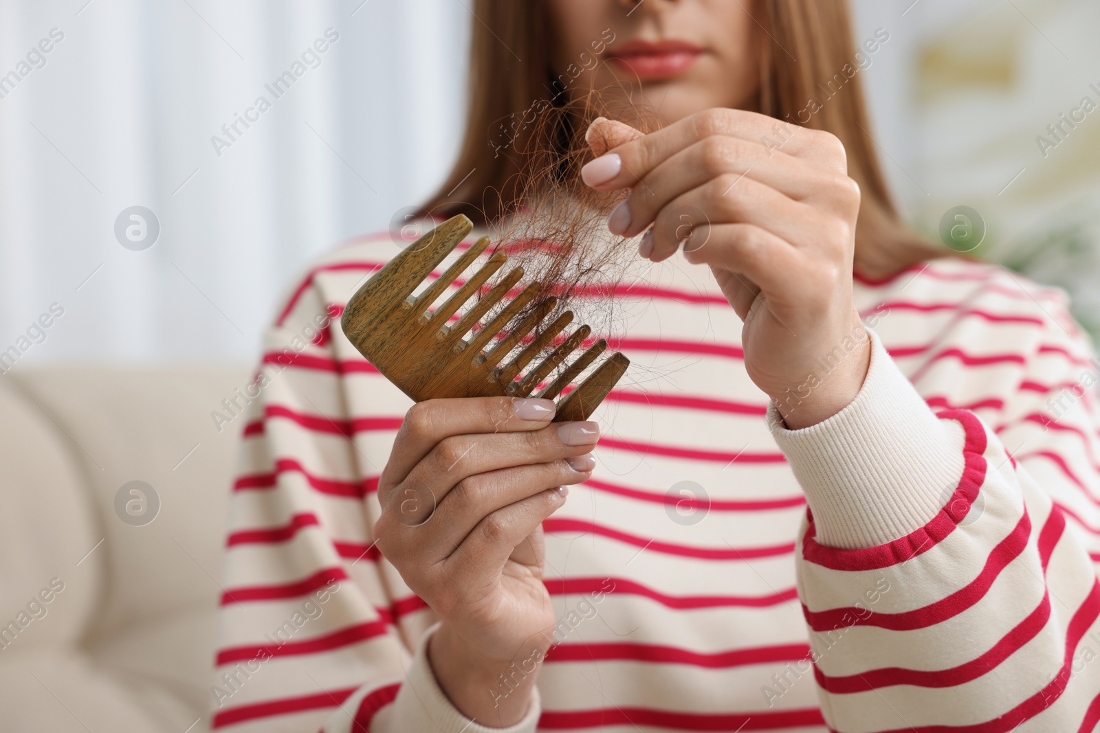 Photo of Woman untangling her lost hair from comb at home, closeup. Alopecia problem