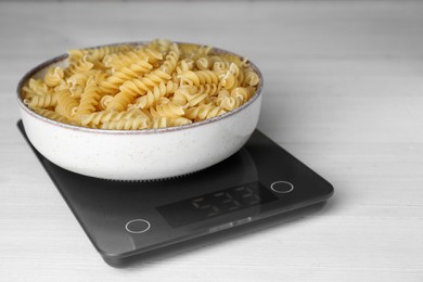 Photo of Electronic scales with uncooked pasta on white wooden table