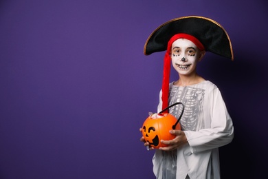 Photo of Cute little boy with pumpkin candy bucket wearing Halloween costume on purple background. Space for text